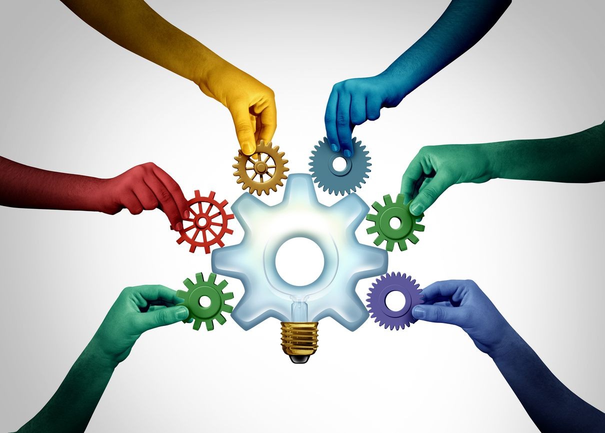 Colored hands holding gears around a light bulb, symbolizing teamwork and innovation.