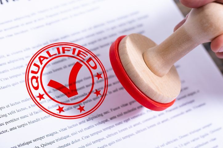 Close-up of a document being stamped with a red 'Qualified' seal and checkmark.