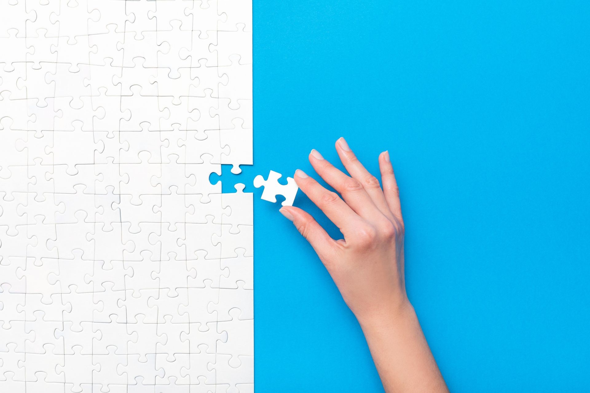 Hand placing final piece in white puzzle on blue background.