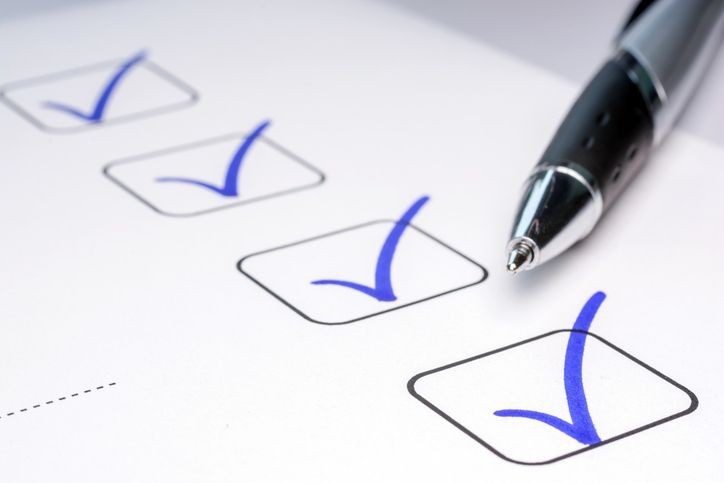 Checklist with blue checkmarks and a pen on a white paper background.