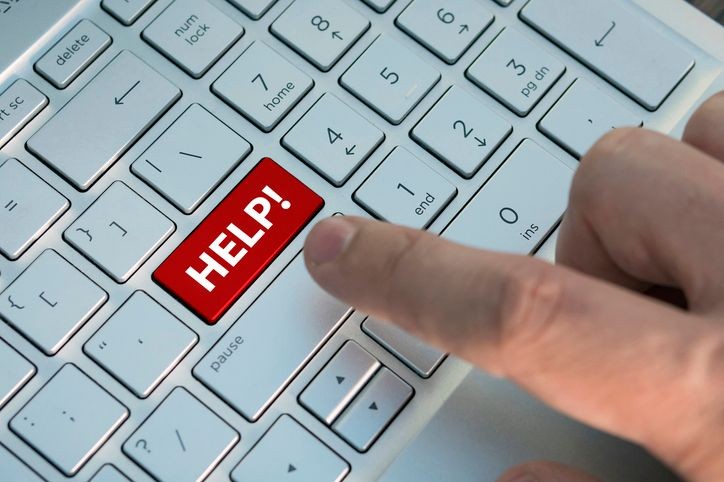 Finger pressing a red 'HELP!' key on a keyboard in place of the enter key.